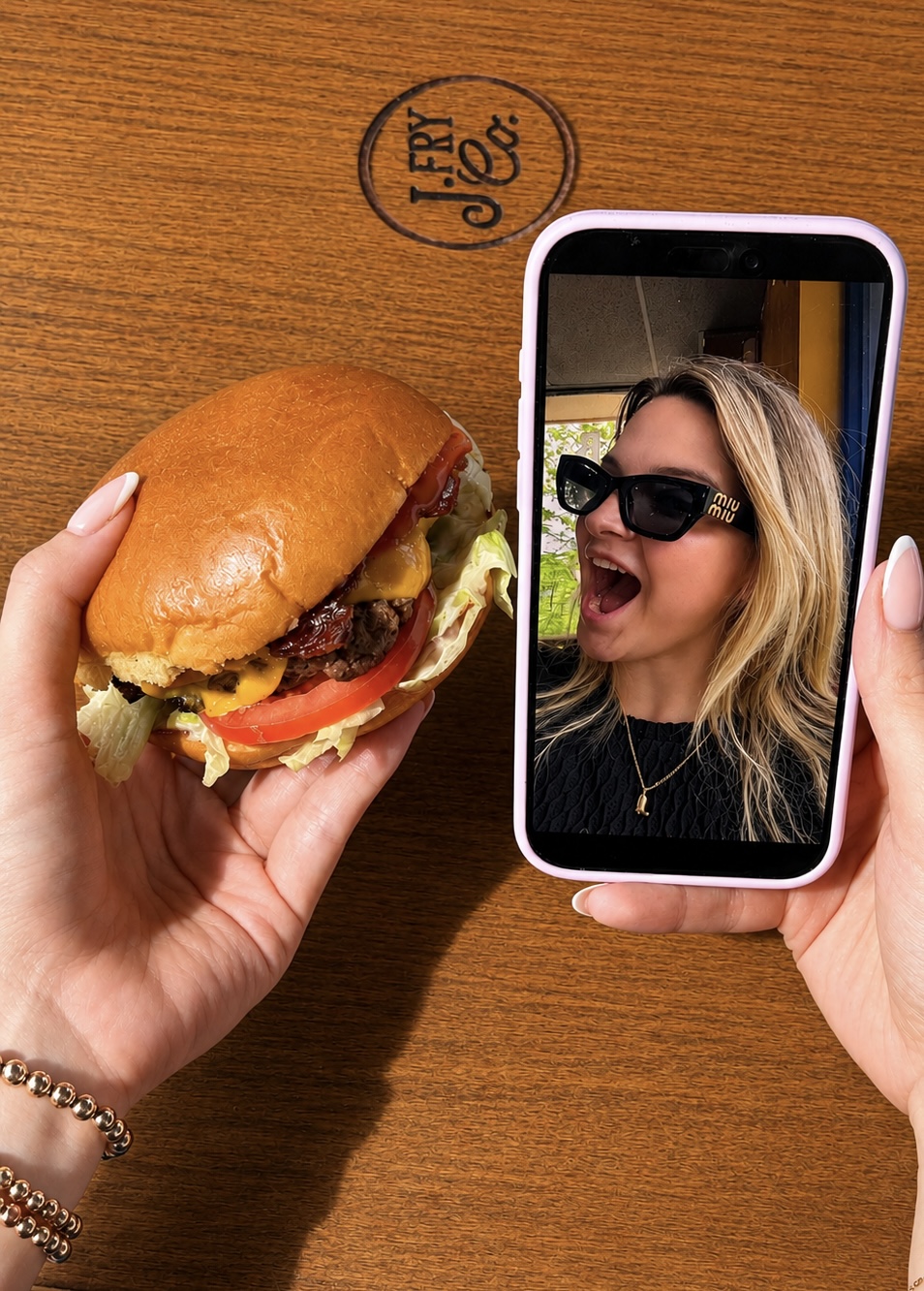 A burger held beside a phone displaying a creator reacting to the meal.